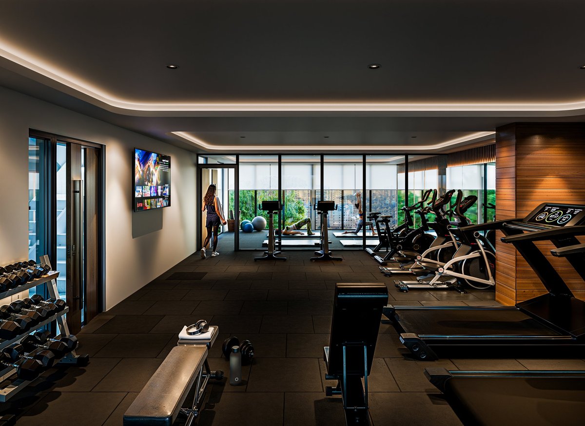 Modern gym interior with treadmills, weights, and exercise equipment overlooking city skyline through large windows