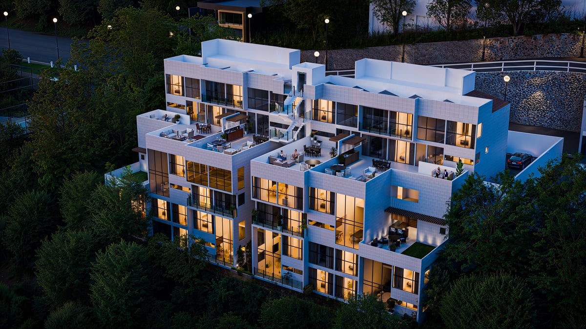 Aerial night view of a modern multi-story residential building with white and blue facade, illuminated windows, and surrounding green landscape.