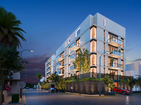 Modern residential apartment building with illuminated balconies at dusk, surrounded by landscaping and parked cars