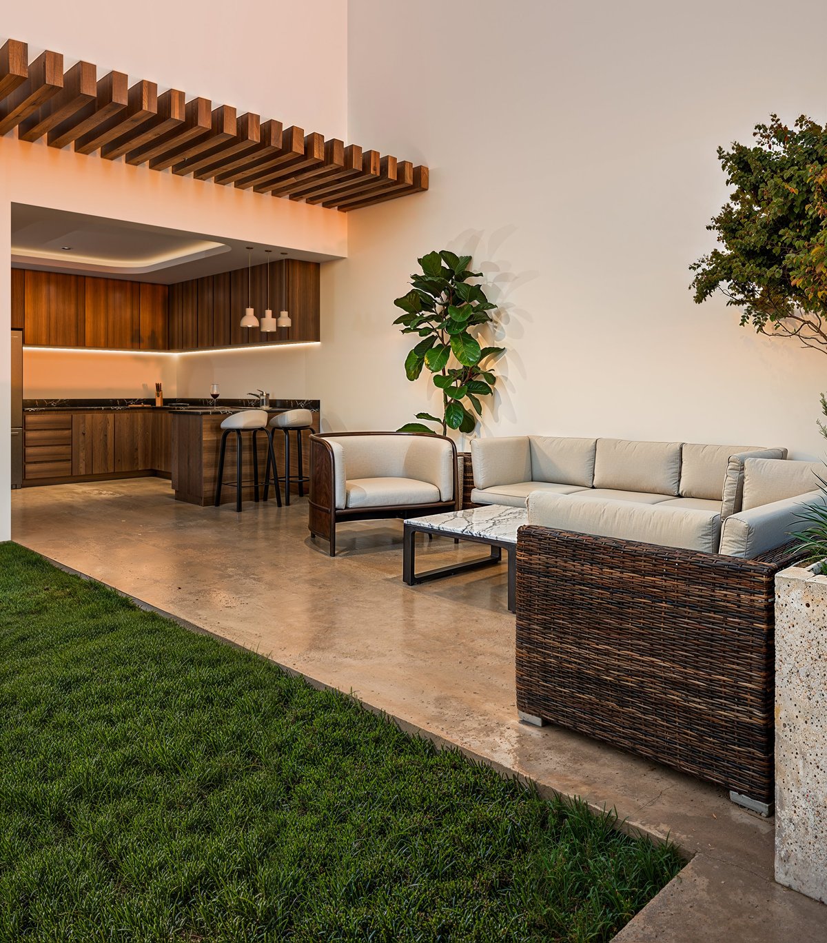 Modern patio with sectional sofa, lounge chair, and wooden pergola overlooking an open kitchen and landscaped lawn