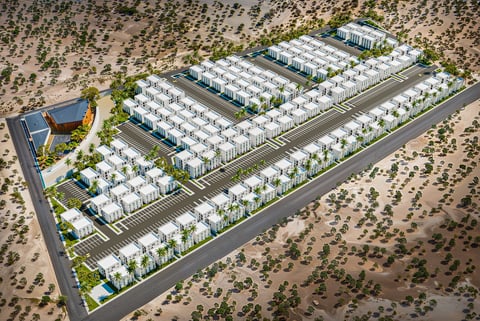Aerial view of a planned residential development with rows of white townhouses on desert land with landscaping and access roads