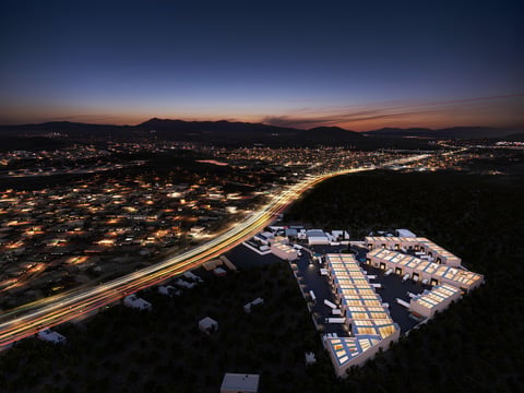 Aerial view of illuminated industrial complex at dusk overlooking a sprawling city at night with glowing streets and distant hills