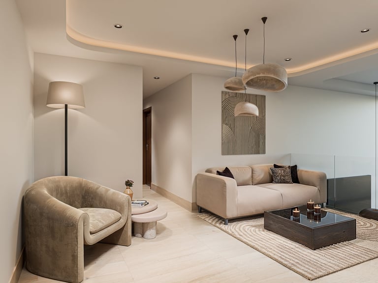 Modern luxury living room with beige sofa, curved accent chair, pendant lighting, and neutral minimalist decor.