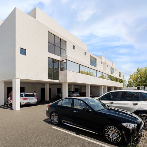 Modern white residential townhouses with garages, featuring cars parked outside under a clear blue sky