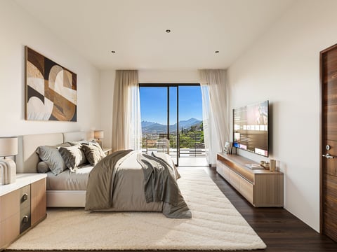 Modern bedroom with beige bedding, wood furnishings, large windows overlooking mountains, TV on dresser, and minimalist decor